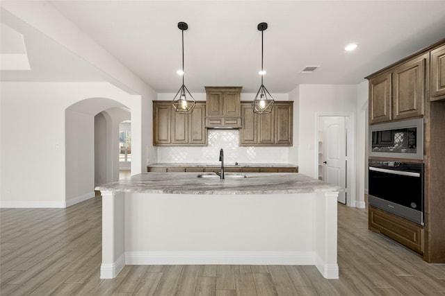 kitchen featuring a kitchen island with sink, decorative light fixtures, sink, oven, and black microwave