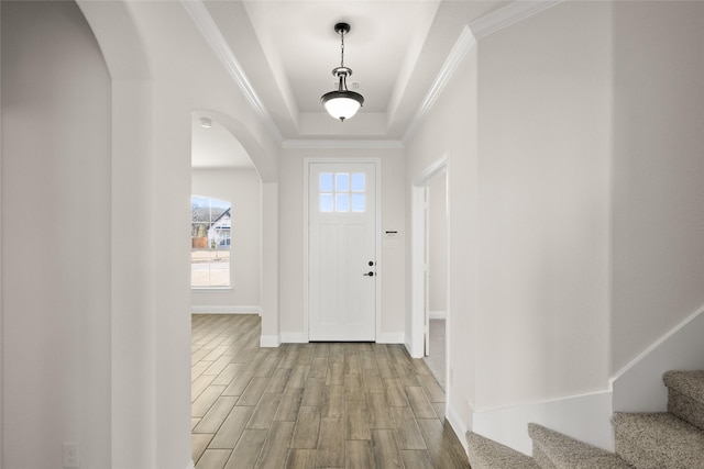 foyer entrance with crown molding, stairs, wood finished floors, a tray ceiling, and arched walkways