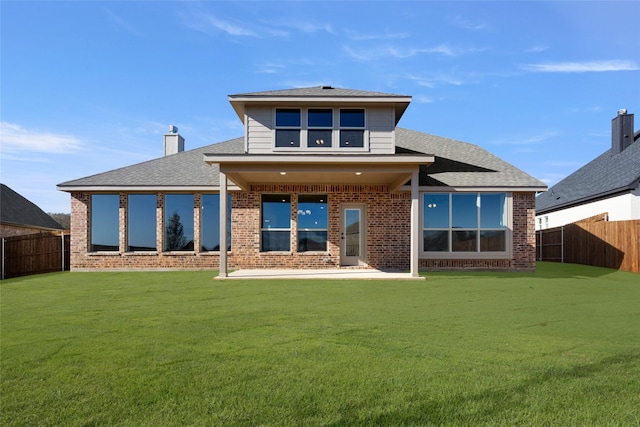back of property featuring a fenced backyard, a yard, roof with shingles, and brick siding