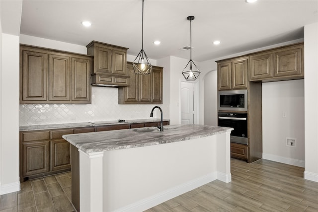 kitchen with built in microwave, a kitchen island with sink, hanging light fixtures, oven, and black electric cooktop