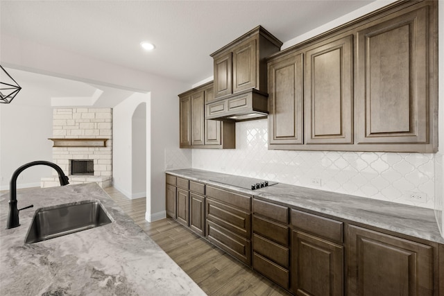 kitchen with black electric cooktop, light hardwood / wood-style floors, decorative backsplash, a fireplace, and sink