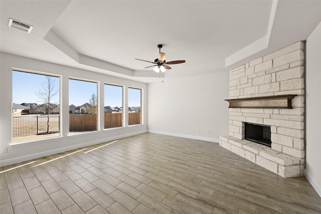 unfurnished living room with a raised ceiling, ceiling fan, baseboards, and visible vents