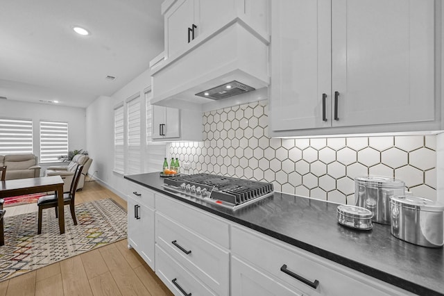 kitchen with premium range hood, stainless steel gas cooktop, white cabinets, and light hardwood / wood-style floors