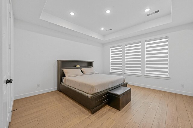 bedroom featuring a raised ceiling and light wood-type flooring