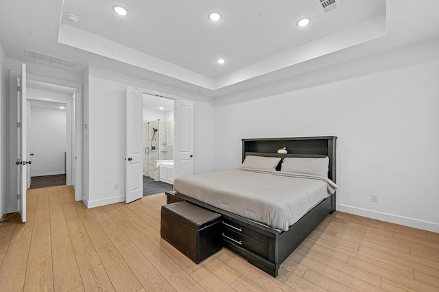 bedroom with light hardwood / wood-style floors, a raised ceiling, and ensuite bathroom