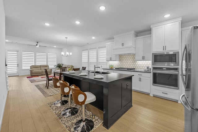 kitchen with appliances with stainless steel finishes, a kitchen island with sink, white cabinets, light hardwood / wood-style floors, and hanging light fixtures