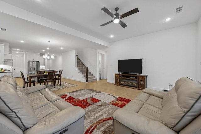 living room featuring ceiling fan with notable chandelier and light wood-type flooring