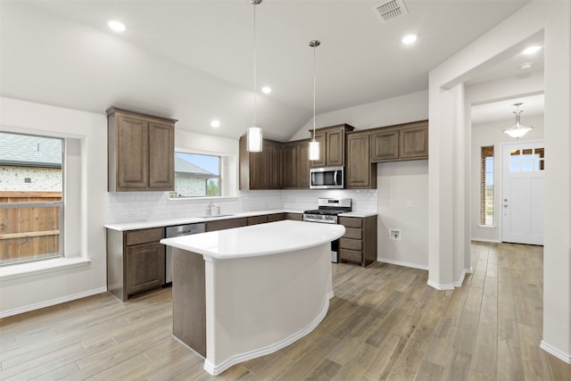 kitchen featuring sink, decorative light fixtures, appliances with stainless steel finishes, a kitchen island, and light hardwood / wood-style floors