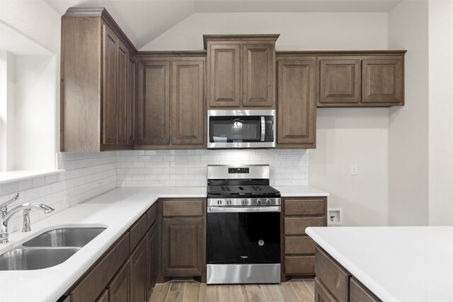 kitchen featuring sink, stainless steel appliances, tasteful backsplash, light hardwood / wood-style flooring, and vaulted ceiling