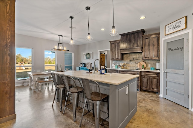 kitchen with light stone counters, a breakfast bar, hanging light fixtures, and a center island with sink