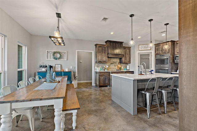 kitchen featuring stainless steel appliances, decorative light fixtures, a kitchen breakfast bar, and an island with sink