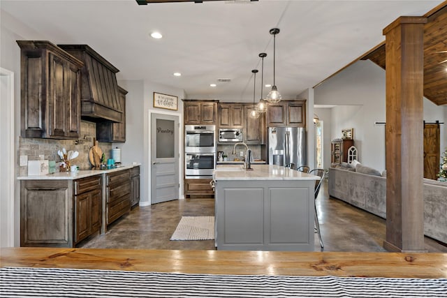 kitchen with decorative light fixtures, appliances with stainless steel finishes, decorative backsplash, and a center island with sink