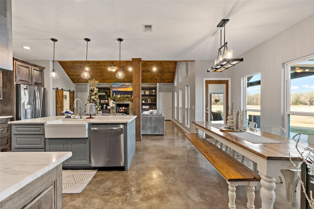 kitchen featuring sink, gray cabinetry, stainless steel appliances, a barn door, and a center island with sink