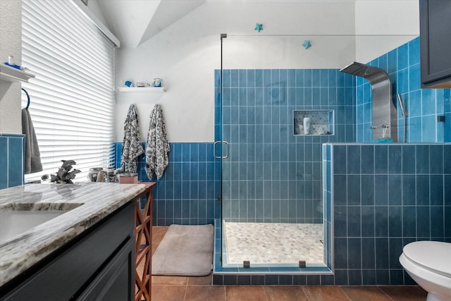 bathroom featuring tile patterned flooring, toilet, a shower with door, tile walls, and vanity