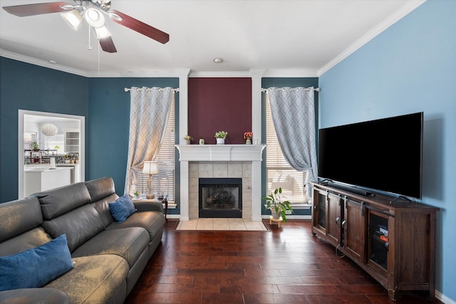 living room with dark wood-type flooring, ceiling fan, crown molding, and a tiled fireplace