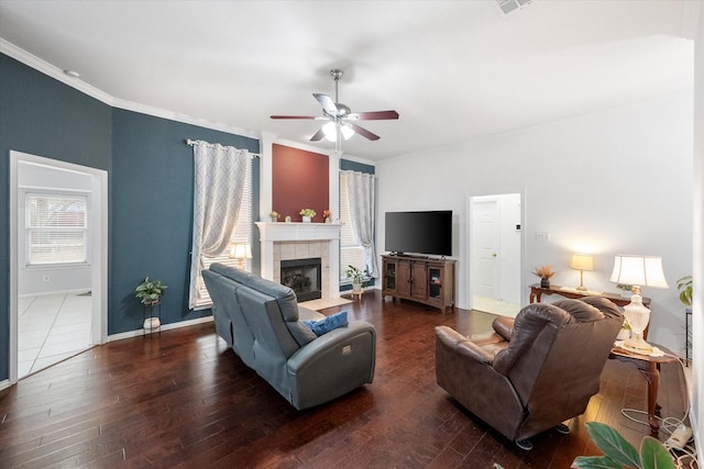 living room featuring ceiling fan, ornamental molding, dark wood-type flooring, and a tile fireplace