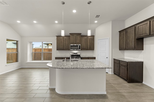 kitchen featuring light stone counters, a center island with sink, lofted ceiling, and appliances with stainless steel finishes