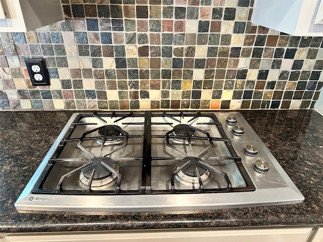 details featuring white cabinetry, decorative backsplash, dark stone counters, and stainless steel gas cooktop