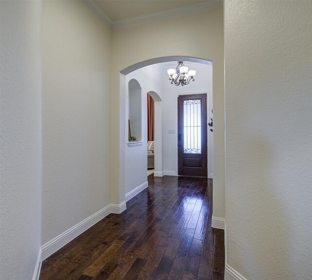 entrance foyer with dark wood-type flooring, ornamental molding, and an inviting chandelier