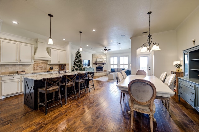 dining room featuring ceiling fan with notable chandelier, dark wood-type flooring, crown molding, and a fireplace