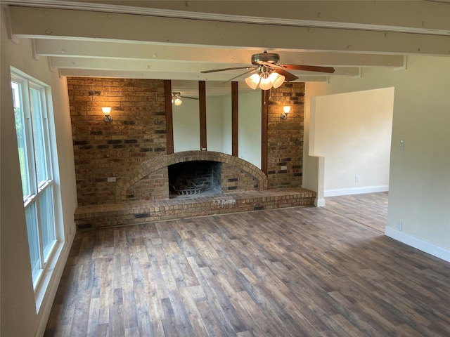 unfurnished living room with dark hardwood / wood-style floors, ceiling fan, a fireplace, beamed ceiling, and brick wall