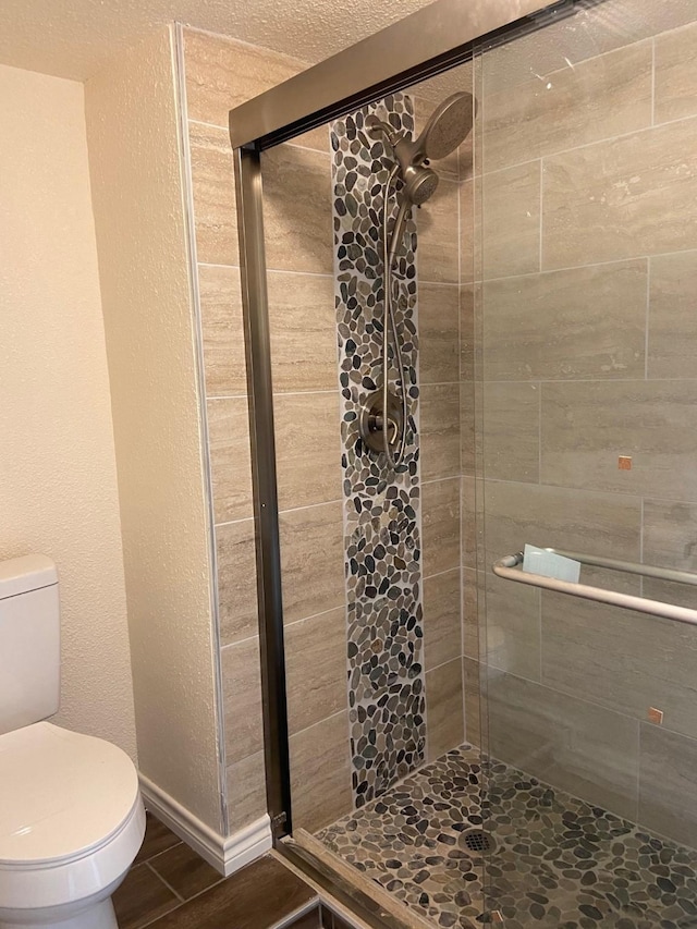 bathroom featuring a textured ceiling, toilet, and a shower with door