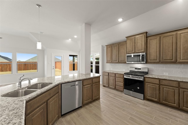 kitchen with light stone countertops, sink, stainless steel appliances, pendant lighting, and decorative backsplash