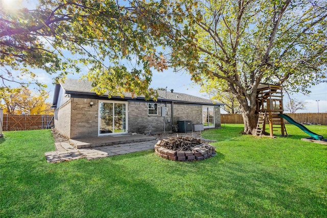 back of house with a fire pit, a lawn, central AC unit, a patio area, and a playground