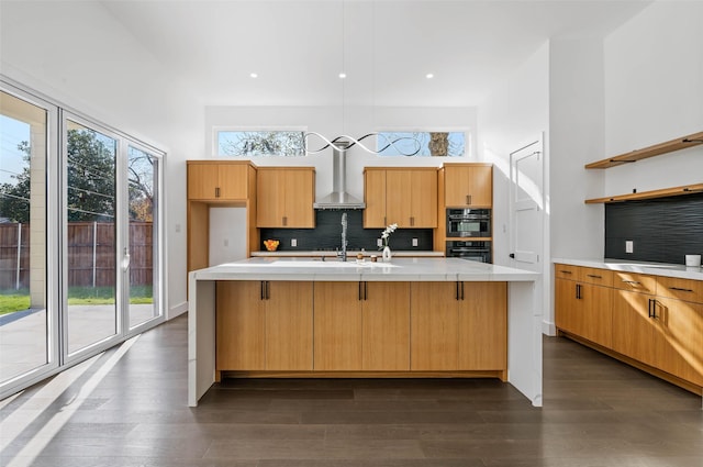 kitchen featuring wall chimney exhaust hood, decorative backsplash, a kitchen island with sink, and dark wood-type flooring