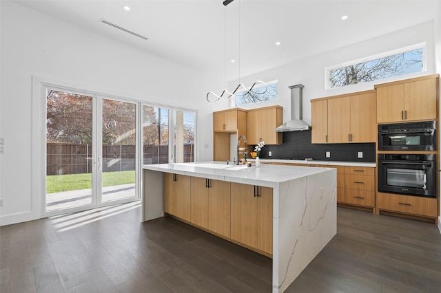 kitchen with pendant lighting, a center island with sink, a healthy amount of sunlight, and wall chimney range hood