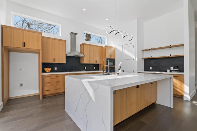 kitchen featuring tasteful backsplash, wall chimney exhaust hood, a kitchen island with sink, dark hardwood / wood-style floors, and black stovetop