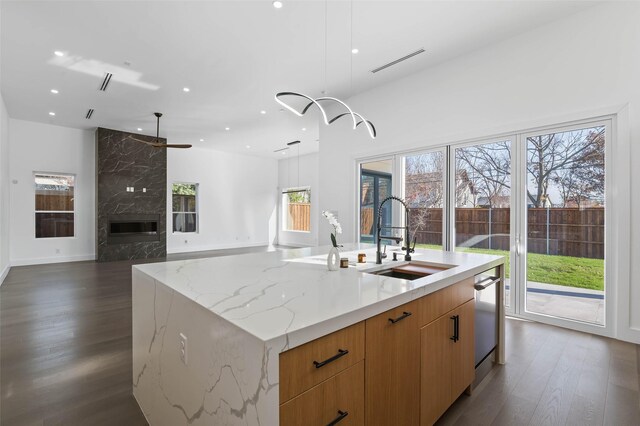 kitchen with a large island, sink, light stone counters, dark hardwood / wood-style flooring, and a high end fireplace