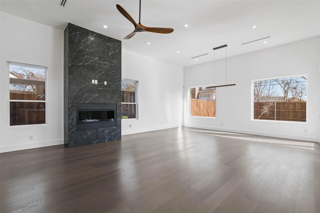 unfurnished living room featuring a premium fireplace, dark hardwood / wood-style flooring, ceiling fan, and a healthy amount of sunlight