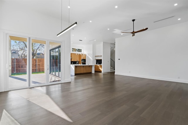 unfurnished living room featuring ceiling fan, dark hardwood / wood-style flooring, and a high ceiling