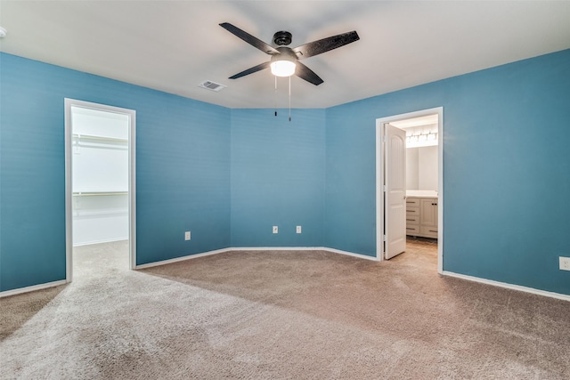 unfurnished bedroom with ensuite bathroom, a spacious closet, light carpet, a closet, and ceiling fan