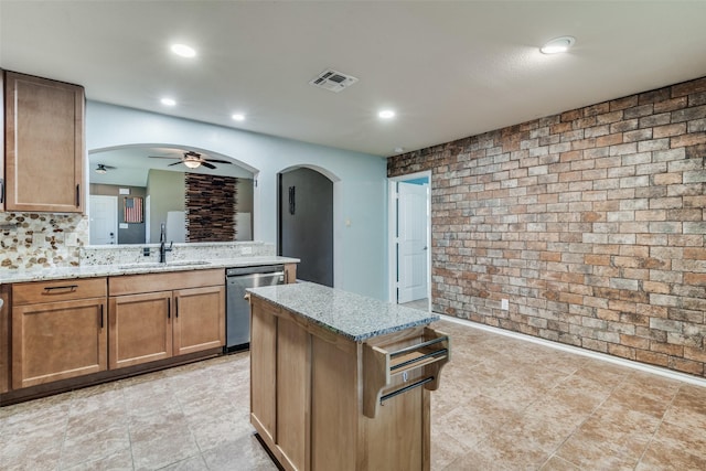 kitchen with light stone counters, sink, dishwasher, and a kitchen island