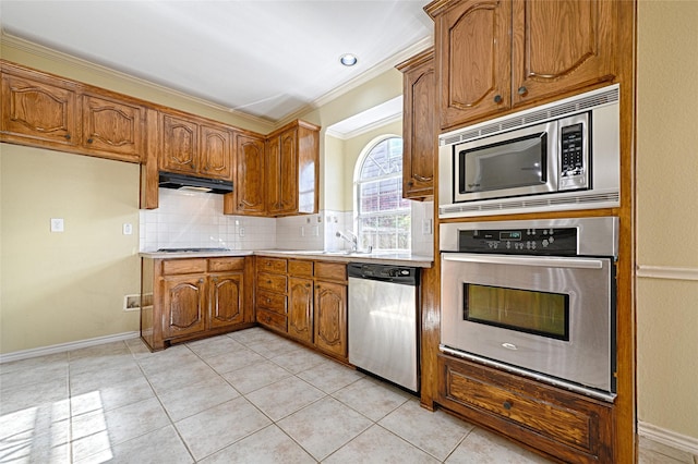 kitchen featuring backsplash, stainless steel appliances, crown molding, sink, and light tile patterned floors