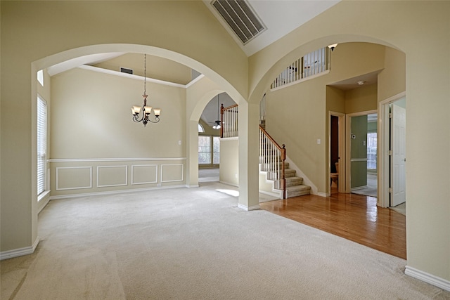 carpeted empty room with high vaulted ceiling and an inviting chandelier