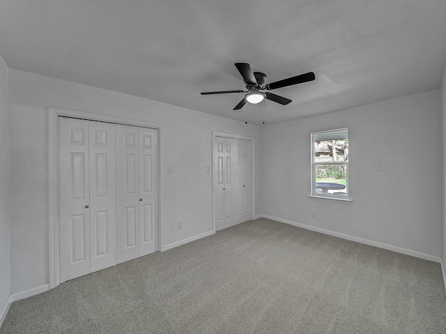 unfurnished bedroom featuring ceiling fan, carpet, and two closets