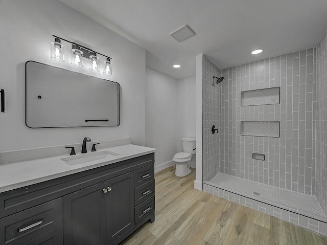 bathroom featuring hardwood / wood-style floors, vanity, toilet, and a tile shower