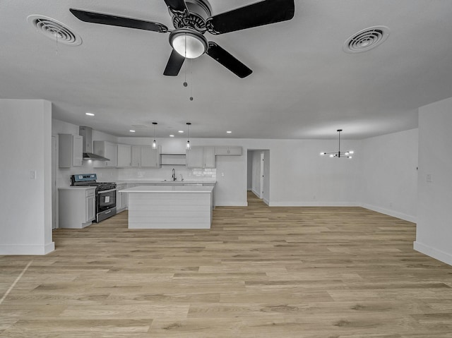 kitchen featuring stainless steel range, sink, light hardwood / wood-style flooring, a kitchen island, and hanging light fixtures