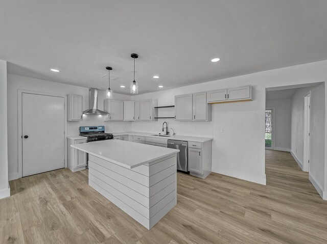 kitchen featuring wall chimney exhaust hood, stainless steel appliances, a center island, light hardwood / wood-style floors, and hanging light fixtures