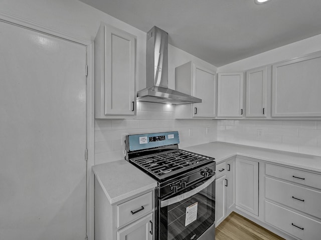 kitchen featuring wall chimney range hood, stainless steel gas range, light wood-type flooring, tasteful backsplash, and white cabinetry