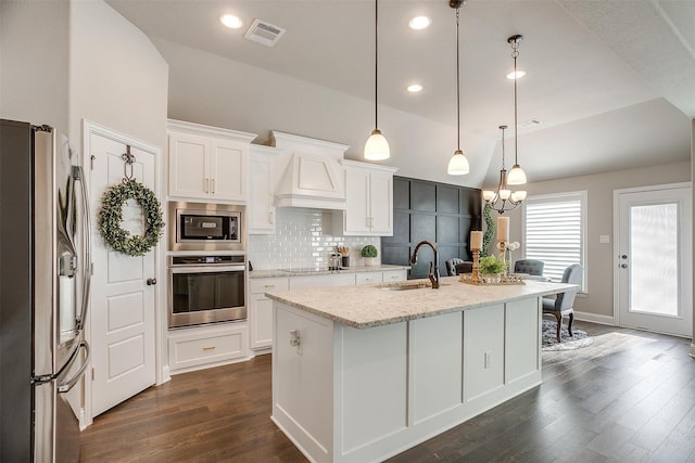 kitchen featuring a center island with sink, custom range hood, light stone counters, white cabinetry, and stainless steel appliances