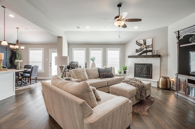 living room featuring a stone fireplace, ceiling fan with notable chandelier, dark hardwood / wood-style floors, and vaulted ceiling