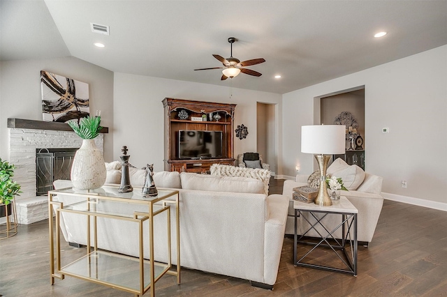 living room featuring a stone fireplace, ceiling fan, dark wood-type flooring, and vaulted ceiling