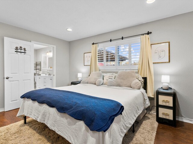 bedroom with ensuite bathroom, dark hardwood / wood-style flooring, and sink