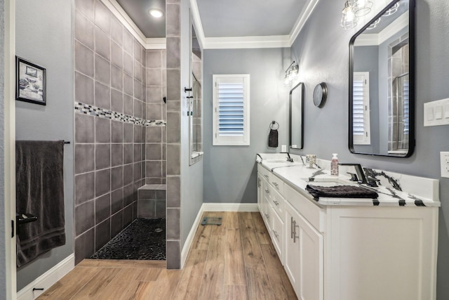 bathroom with wood finished floors, baseboards, ornamental molding, double vanity, and walk in shower