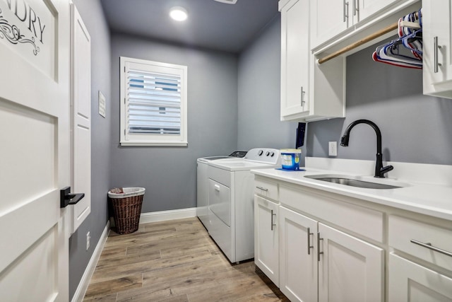 laundry room with cabinets, washing machine and clothes dryer, sink, and light wood-type flooring