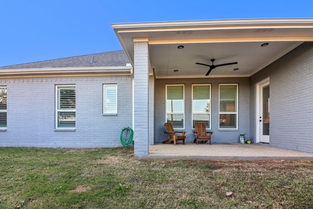 exterior space with a lawn, ceiling fan, roof with shingles, a patio area, and brick siding